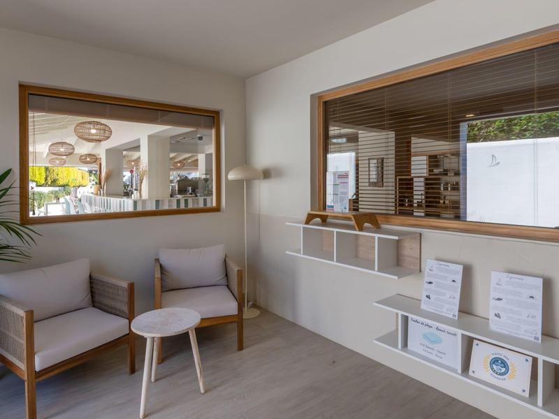 Bright waiting room with gray chairs, small wooden table, plants, and modern shelving.