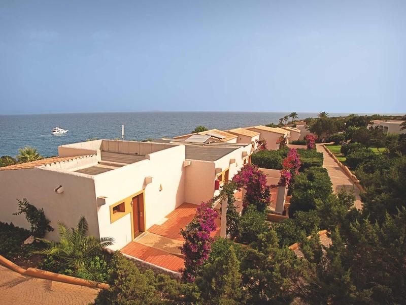 Rijhuizen met witte muren en rode daken in een tuin met uitzicht op zee.