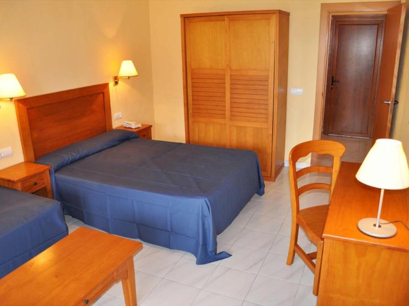 Een eenvoudig ingericht hotelkamer met twee bedden, een bureau en een houten kledingkast.