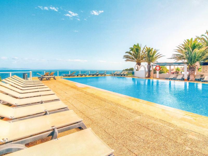 Moderne buitenzwembad met ligstoelen en zeezicht onder een blauwe lucht.
