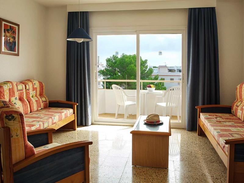 Helles Wohnzimmer mit zwei gemusterten Sofas, Holztisch und großen Fenstern mit Blick auf Balkon und Bäume.