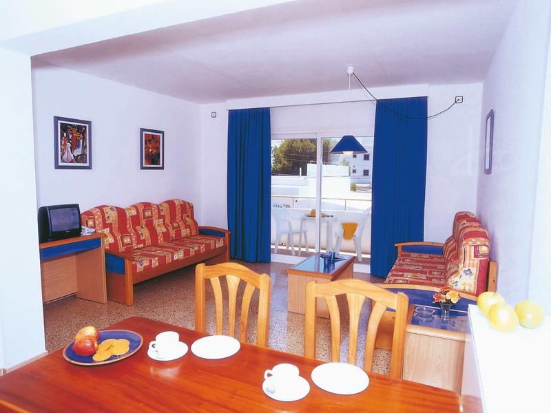 Wohnzimmer mit roten Sofas, blauem Vorhang, Holztisch und Fernseher, Balkon im Hintergrund.