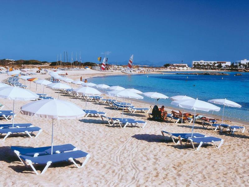 Strand mit weißen Sonnenschirmen, Liegen und klarem blauem Wasser unter blauem Himmel.