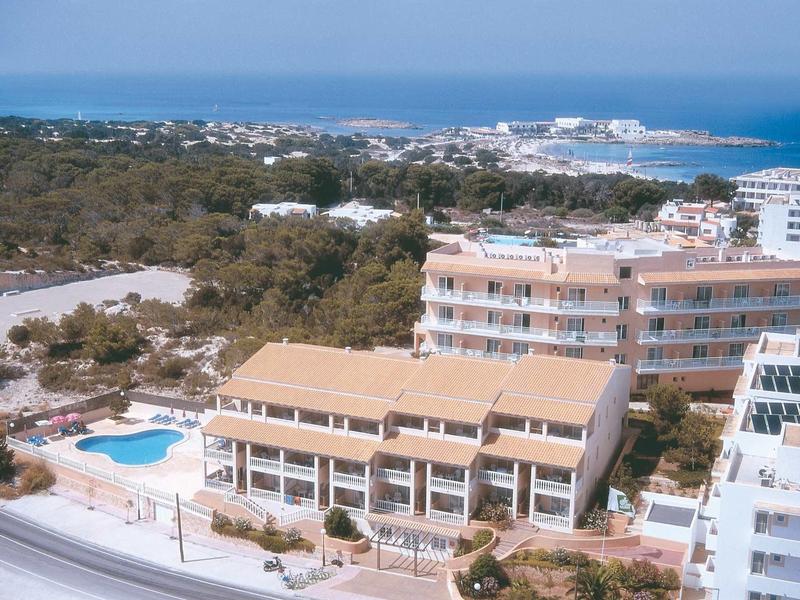 Vista di un hotel con piscina, circondato da alberi e il mare sullo sfondo.