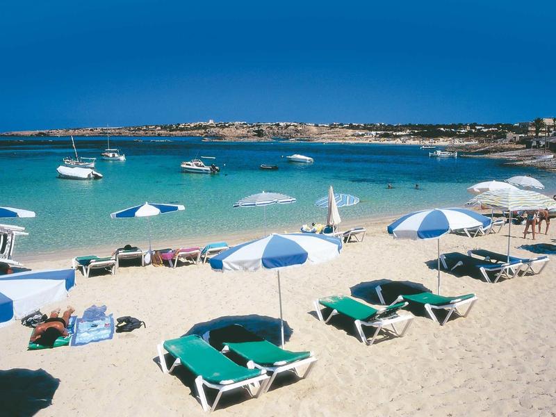 Spiaggia con lettini verdi, ombrelloni blu e bianchi e acqua limpida azzurra.