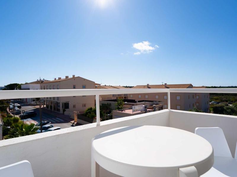 Vista da una terrazza bianca con tavolo rotondo e sedie su case e mare sotto un cielo azzurro.