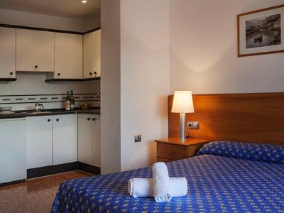 Habitación de hotel con cama azul estampada, cabecero de madera, lámpara de mesa de noche y cocina integrada.