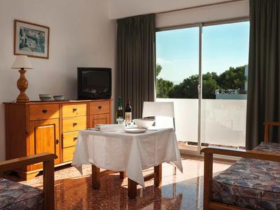 Habitación de hotel con mesa en el centro, televisor y puertas corredizas que dan a un balcón.