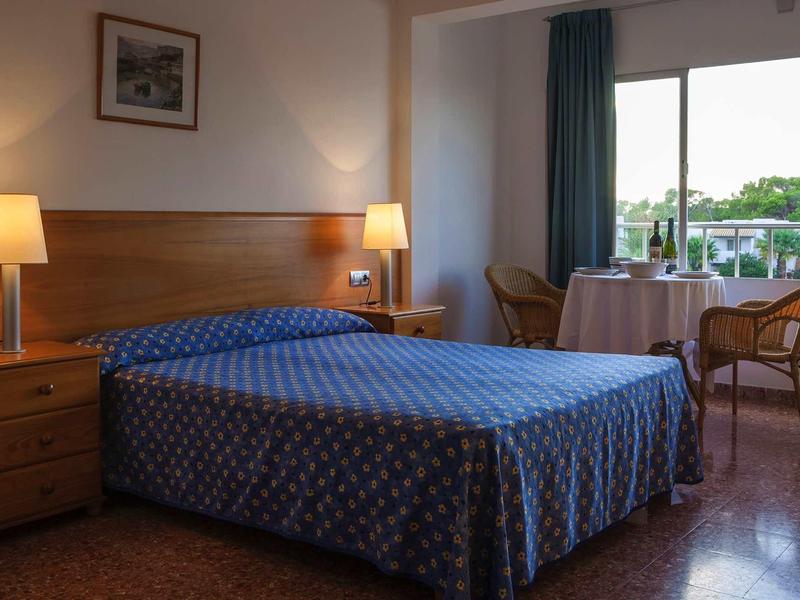 Habitación de hotel acogedora con cama doble, mesitas, lámparas y balcón con vista al jardín.