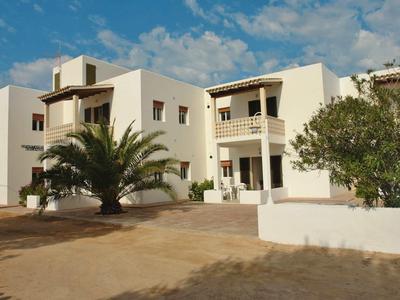 Białe domy wakacyjne z balkonami, palmami i wybrukowanym dziedzińcem pod niebieskim niebem.