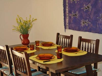 Esszimmer mit dunklem Holztisch, vier Stühlen, gelben Platzsets und rotem Geschirr, Wanddeko und Vase.