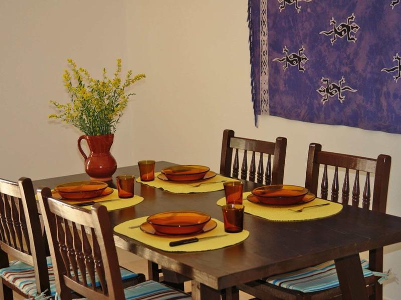 Esszimmer mit dunklem Holztisch, vier Stühlen, gelben Platzsets und rotem Geschirr, Wanddeko und Vase.