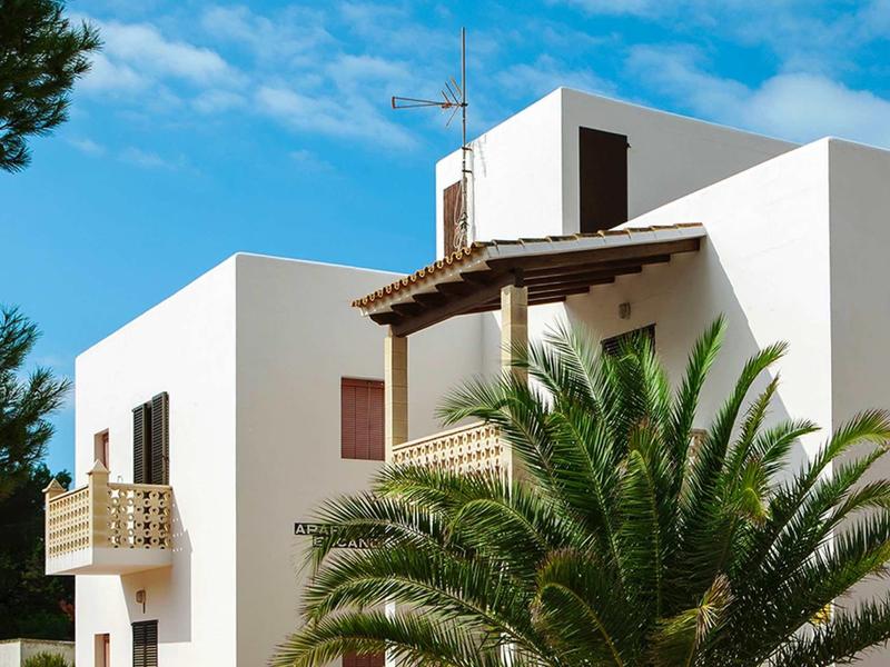 Moderne weiße Gebäude mit Balkon und Palmen vor blauem Himmel und Wolken.