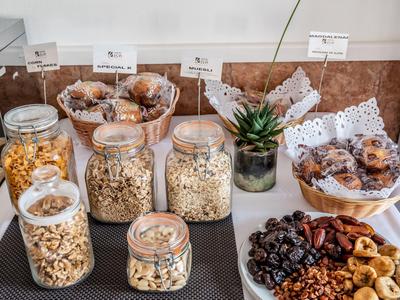 Frühstücksbuffet mit verschiedenen Nüssen, Trockenfrüchten, Popcorn und Muffins in Gläsern und Schalen.