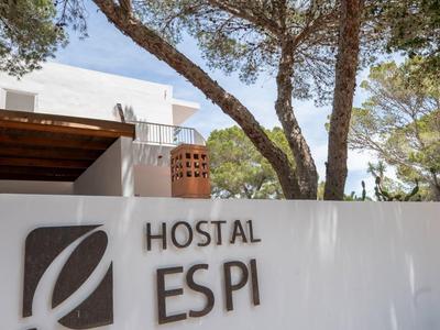 Weiße Mauer mit Hostal ESPI Schriftzug und Bäumen im Hintergrund bei sonnigem Wetter.