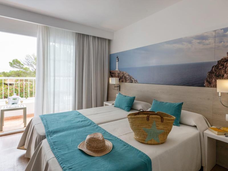 Helles Hotelzimmer mit Doppelbett, blauer Dekoration und Balkon mit Meerblick.