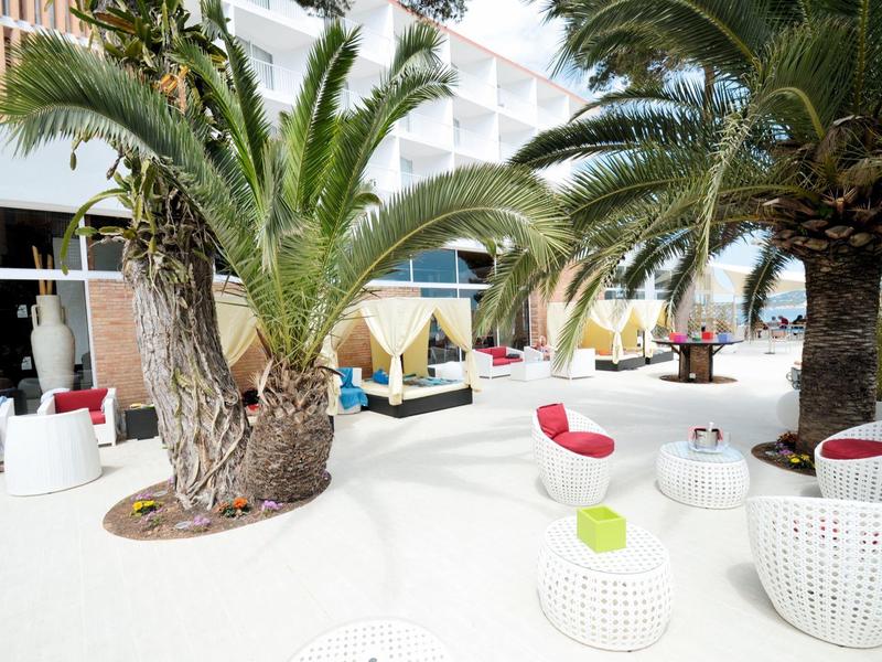 Moderní venkovní lounge s bílým nábytkem a palmami, ideální pro relaxační dovolenou.