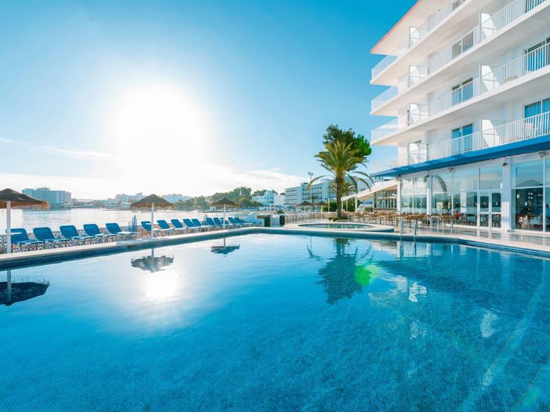 Vytápěný bazén před moderním hotelem s lehátky a palmami při východu slunce.