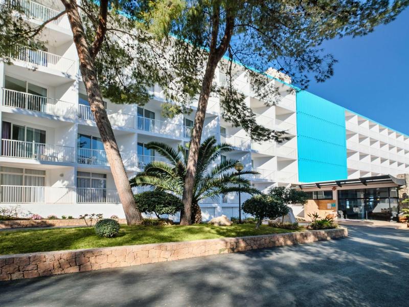 Moderní hotelová budova s balkony a modro-bílou fasádou pod jasnou oblohou.