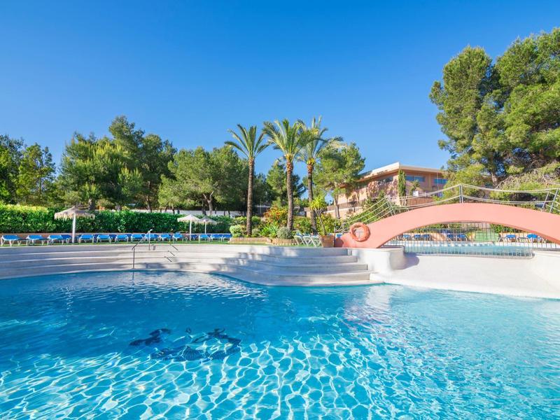 Bazén s tyrkysovou vodou, mostem a lehátky pod čistou oblohou.