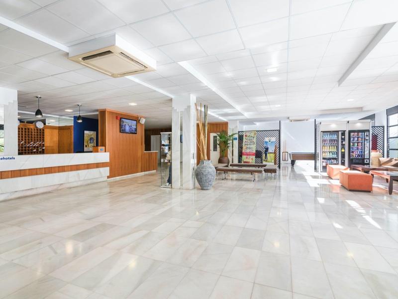 Světlá hotelová lobby s bílou mramorovou podlahou, recepcí a posezením s pohovkou a židlemi.