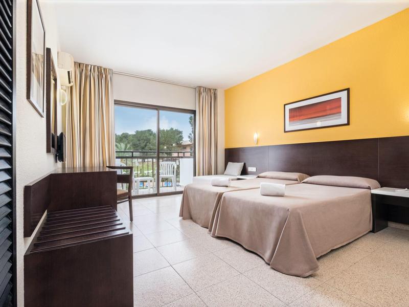 Hotelový pokoj se dvěma jednolůžky, žlutou zdí a balkonem s výhledem.