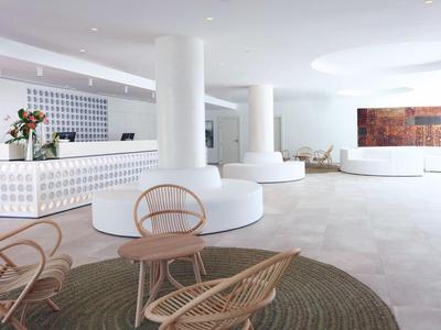 Lichte, moderne hotellobby met wit meubilair en rieten stoelen op een beige vloer