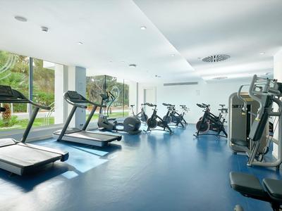 Palestra moderna con tapis roulant e macchine da allenamento vicino a grandi finestre con vista sul verde.