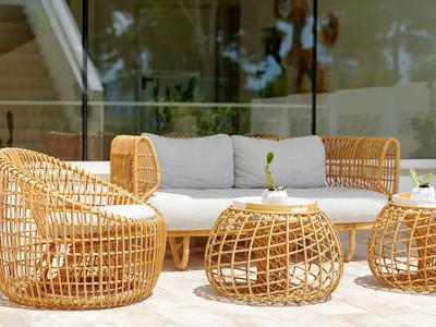 Buitenlounge met gevlochten rotan zitmeubilair, waaronder bank, stoelen en tafels.