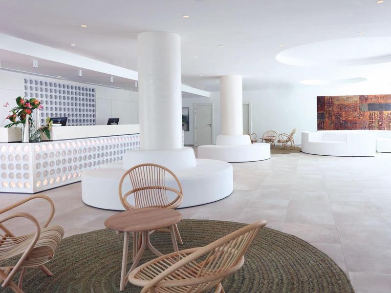 Lichte, moderne hotellobby met wit meubilair en rieten stoelen op een beige vloer