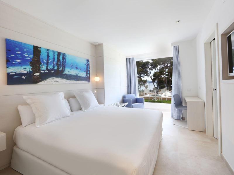 Modern hotelkamer met groot tweepersoonsbed en uitzicht op tuin.