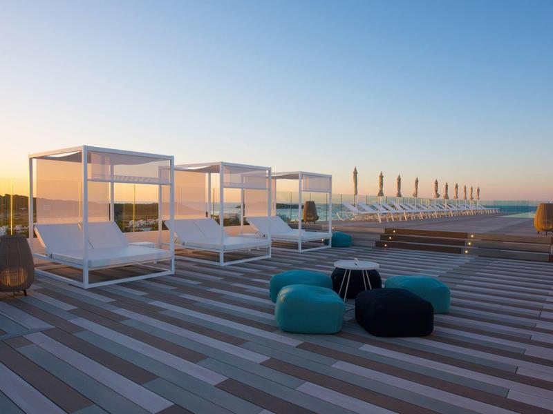 Moderne buitenlounge met bedden en zitzakken op een terras met uitzicht op zee bij zonsondergang.