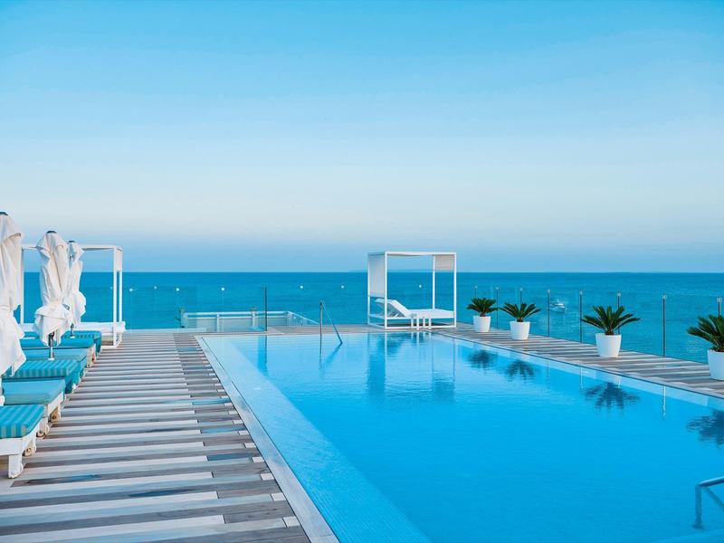 Moderne infinity pool met ligstoelen en zeezicht onder heldere hemel.