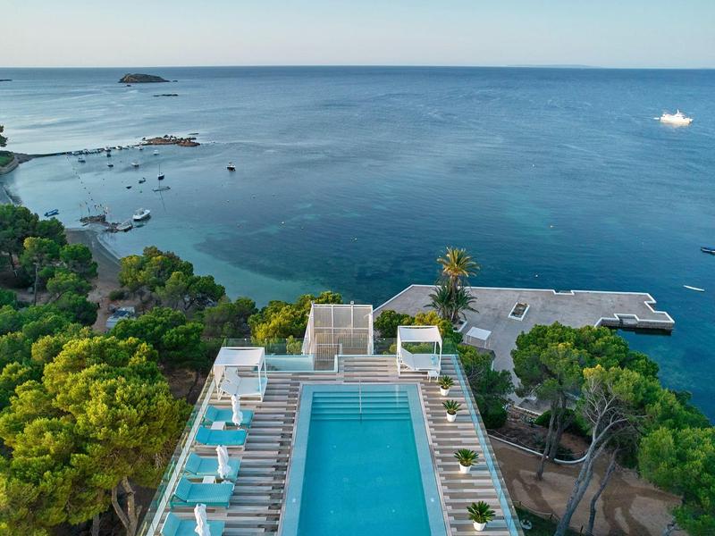 Modern zwembad met ligstoelen aan de kust met blauwe zee en boten.