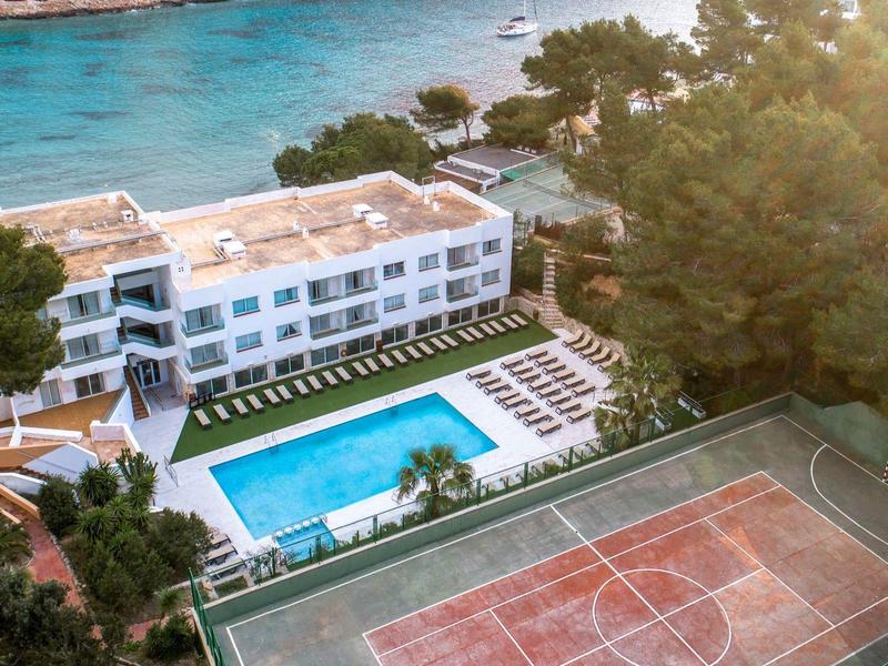 Hotel with outdoor pool, sun loungers, and basketball court near the sea.