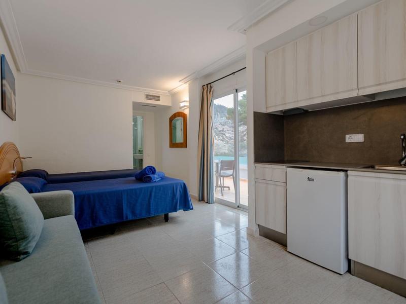 Small hotel room with kitchenette, blue bed, and balcony access.