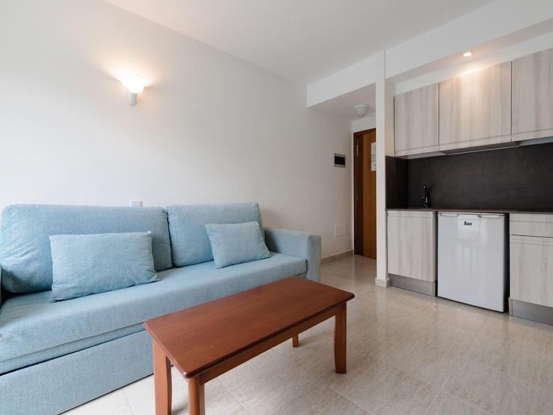 Bright living area with blue sofa, wooden table, and small kitchenette.