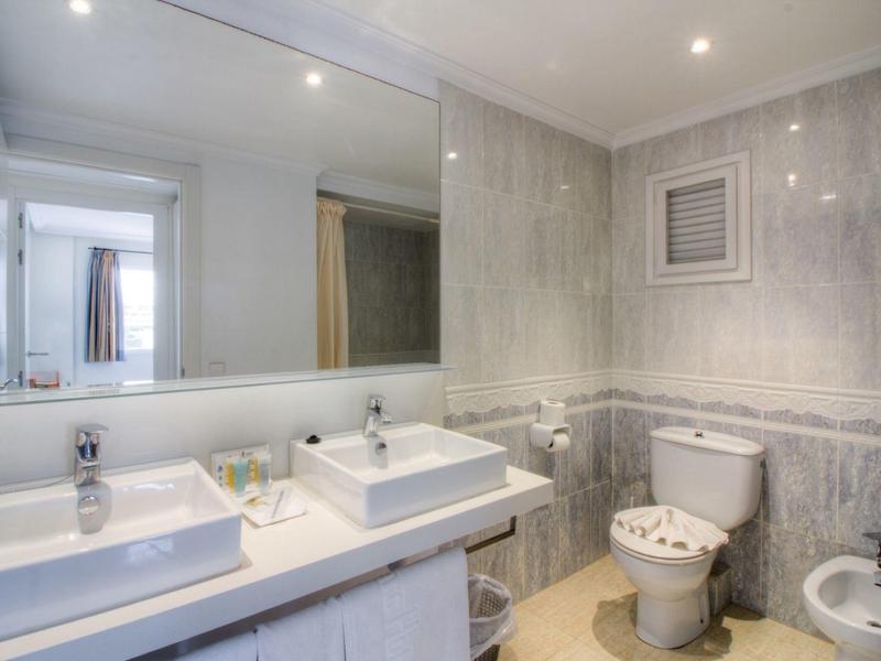 Modern bathroom with two sinks, large mirror, and toilet in neutral tones.