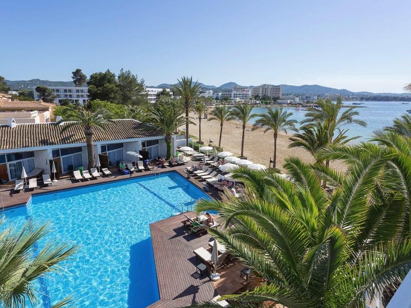 Venkovní bazén se lehátky a výhledem na pláž a moře v pozadí.