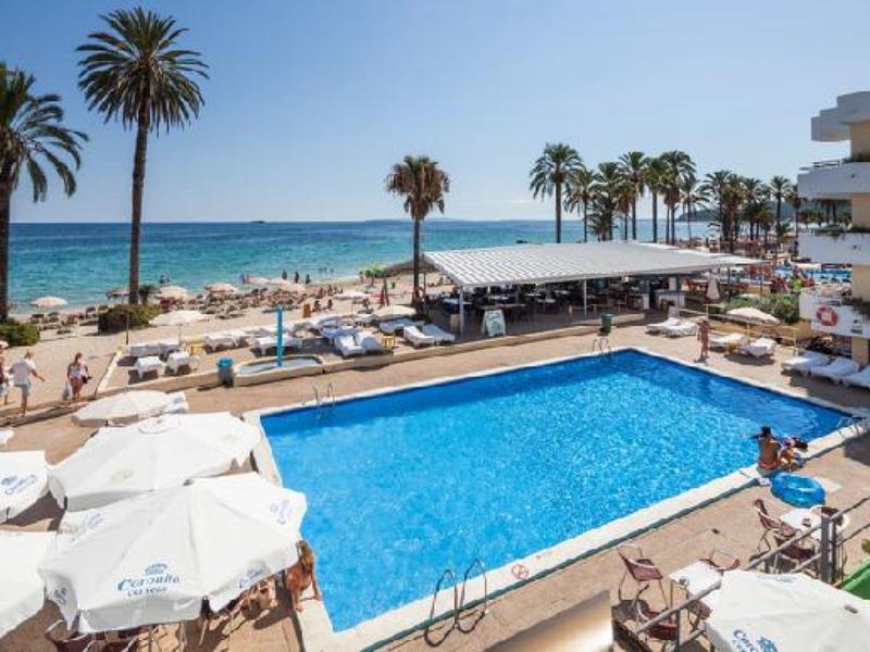 Klares blaues Schwimmbecken mit weißen Liegestühlen, Palmen und Meer im Hintergrund an sonnigem Tag.