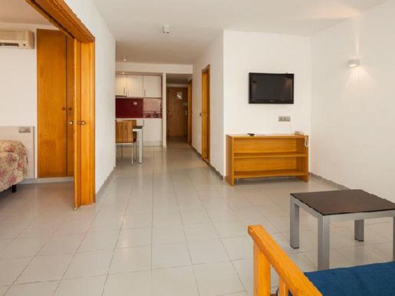 Moderner, heller Wohnraum mit Fliesenboden, Holzmöbeln, offener Küche und angrenzendem Schlafzimmer.