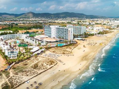 Beach resort with hotels along a wide sandy beach and blue sea under a partly cloudy sky.