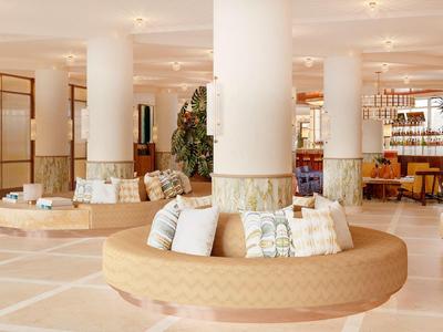 Bright, modern hotel lounge area with circular seating around columns and decorative plants.