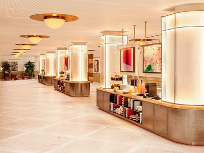 Brightly lit hotel corridor with modern pillars and decorative light fixtures.