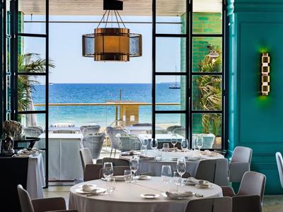 Elegant restaurant with sea view and large windows, stylishly set tables and gray chairs.