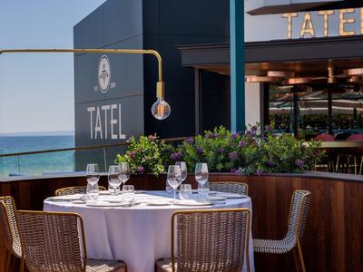 Elegant table with white tablecloths and glasses on a terrace overlooking the sea and restaurant.
