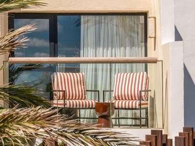 Two striped chairs and a small table on a balcony with glass railing in daylight.