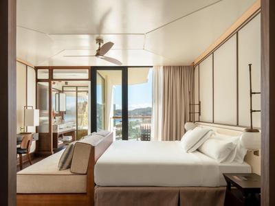 Modern hotel room with large double bed, wooden furniture, and view of terrace and mountains.