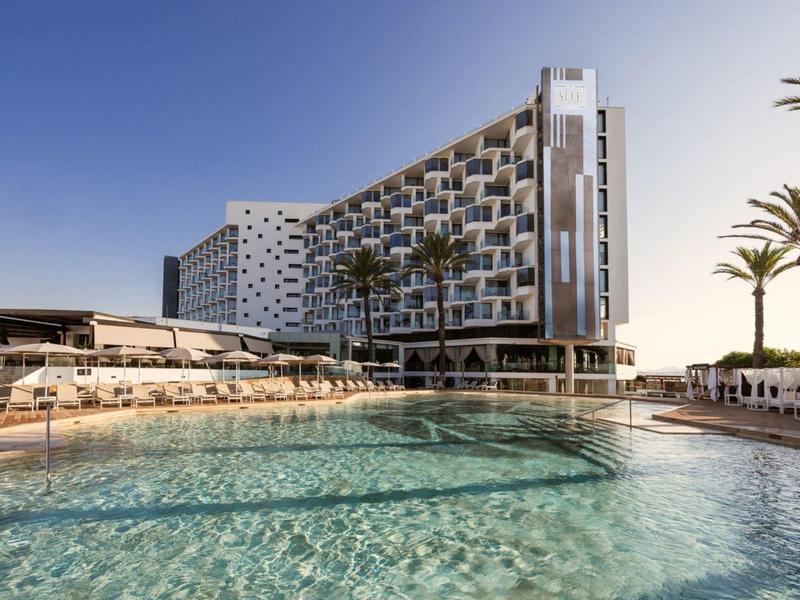 Modern hotel building with swimming pool and sun umbrellas under clear sky