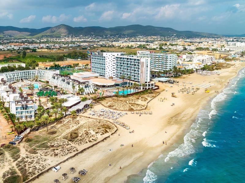 Beach resort with hotels along a wide sandy beach and blue sea under a partly cloudy sky.
